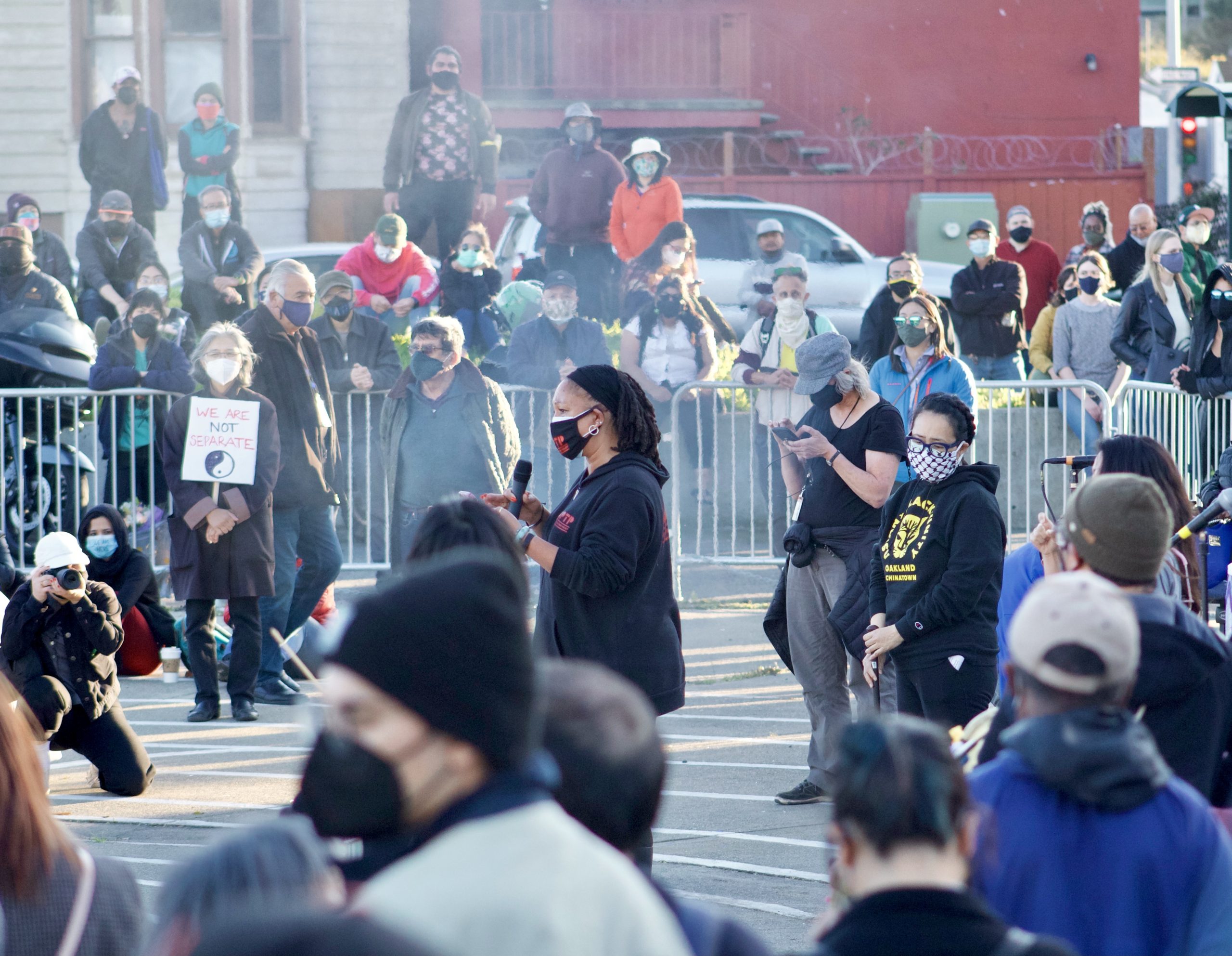 An African American woman wearing all black speaks at a vigil in Oakland.