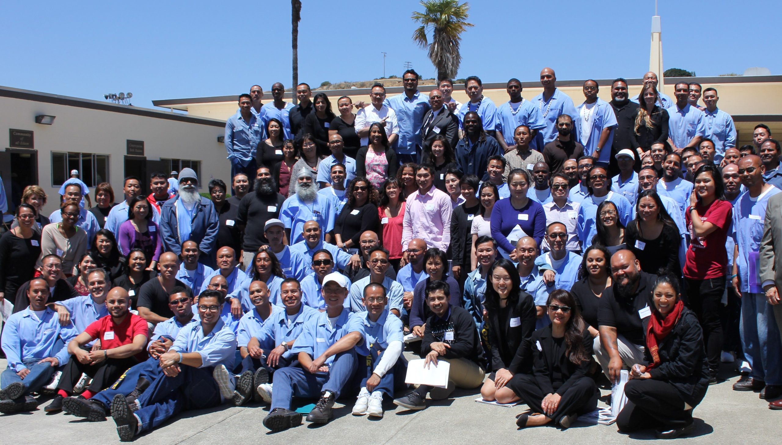Outside, a large group of people wearing blue garb gather for a photo, including some elected officials and staff from APSC.