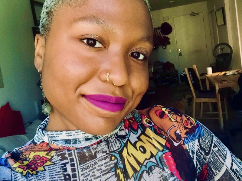 A Guyanese American woman with short blond hair and a brightly colored shirt smiles at camera