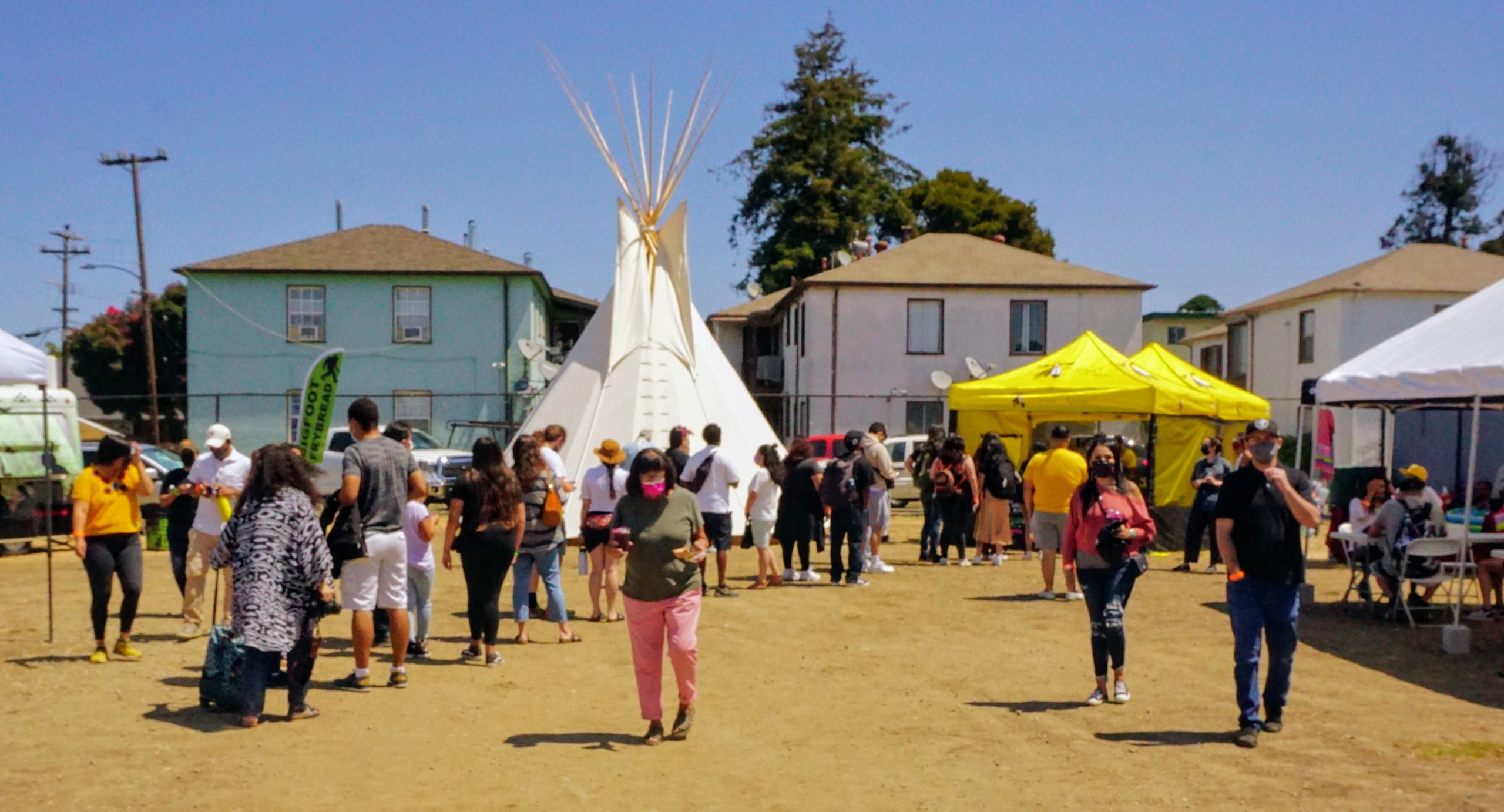 People are milling around outside at an open-air market focusing on Native vendors and services