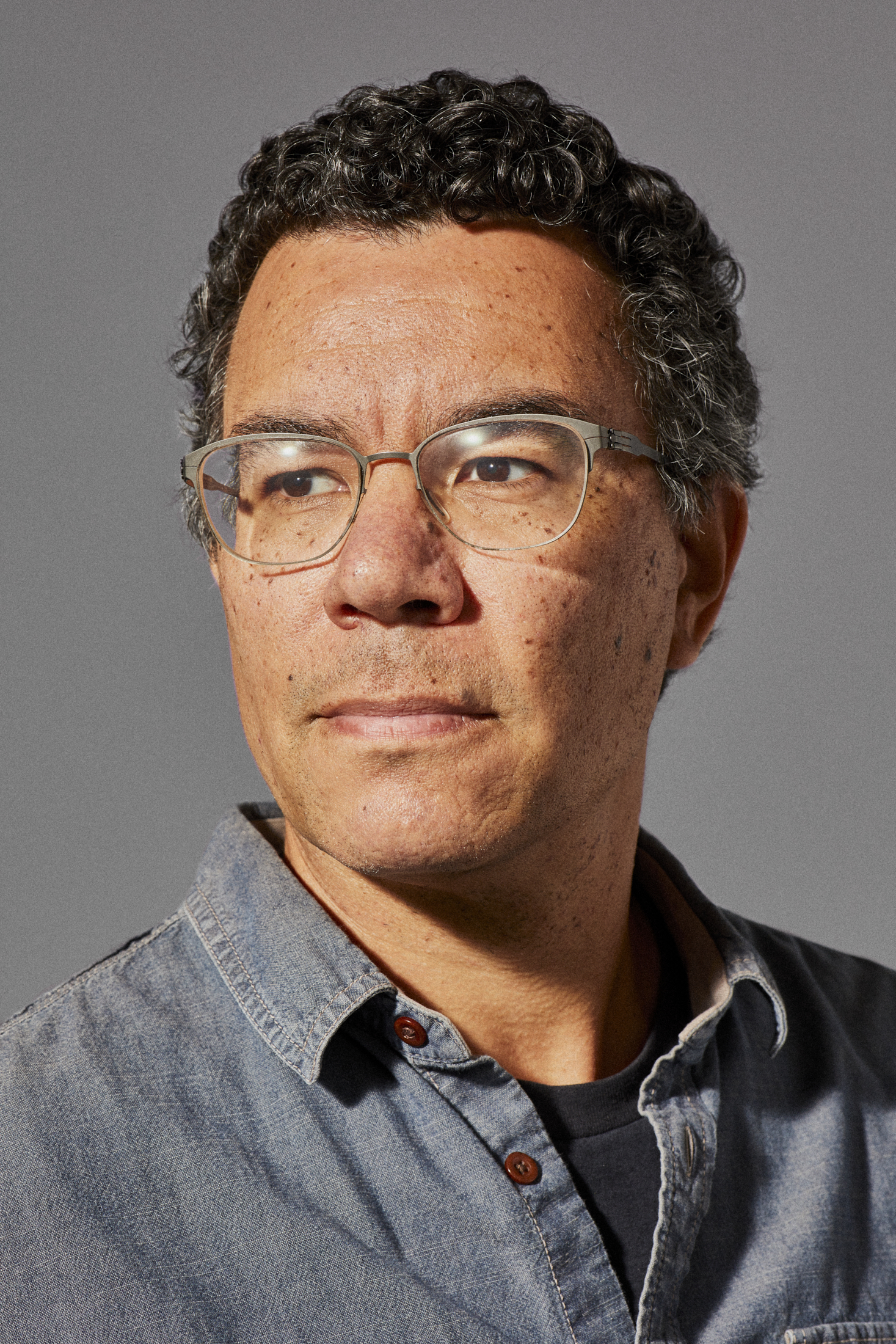 A middle aged man wearing glasses looks into the distance in his headshot.