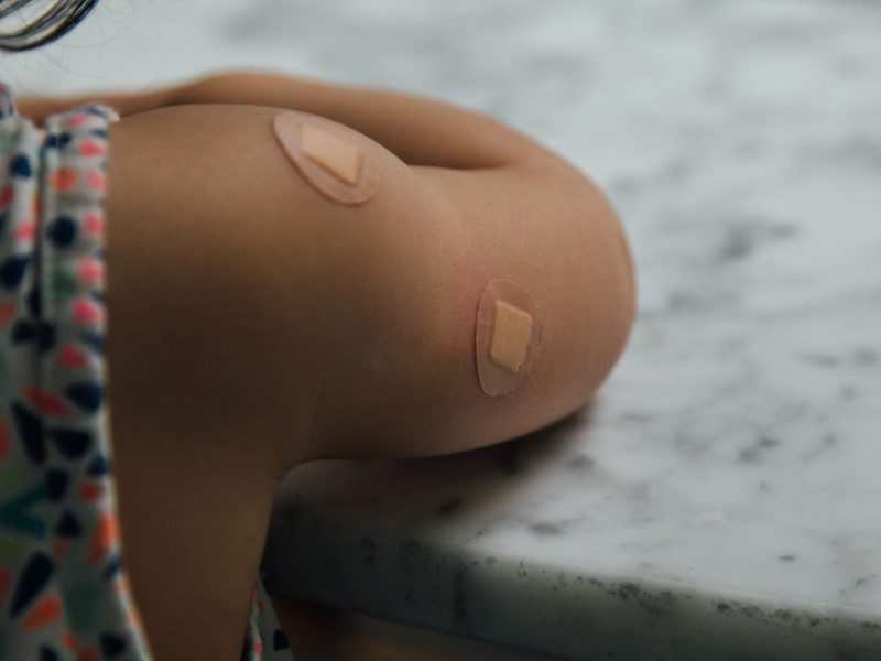a kid's arm with small bandaids to cover where they got a shot