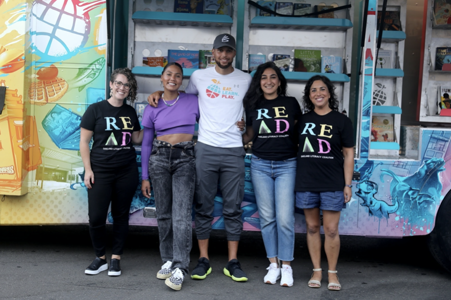 Several smiling people stand casually in front of a colorful mobil bus.