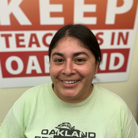 A Latina man with a smile stands in front of a union sign supporting OUSD teachers.