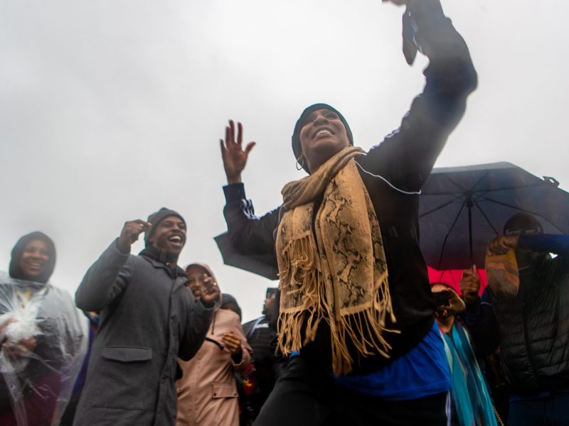 An African American woman dances joyfully against an overcast backdrop and in the rain