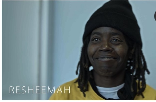 A Black woman wearing a beanie is holding back a smile.
