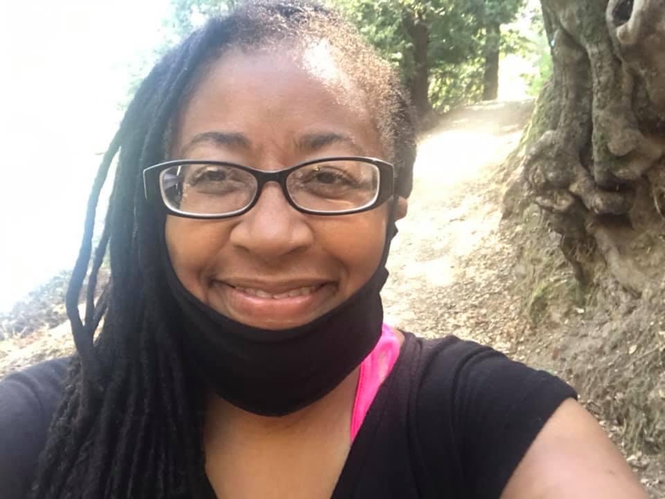 A smiling woman with braids and glasses takes a selfie outside
