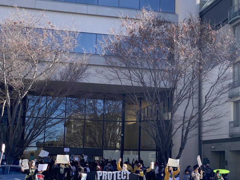 a large group holds a sign facing traffic "Protest Oakland Schools"