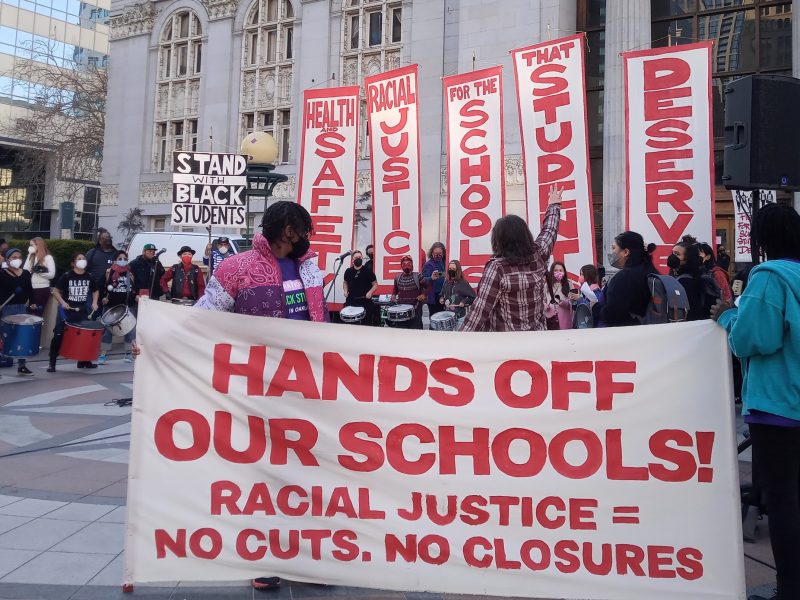 A banner that says "hands off our schools" in bold red letters in front of Oakland City Hall