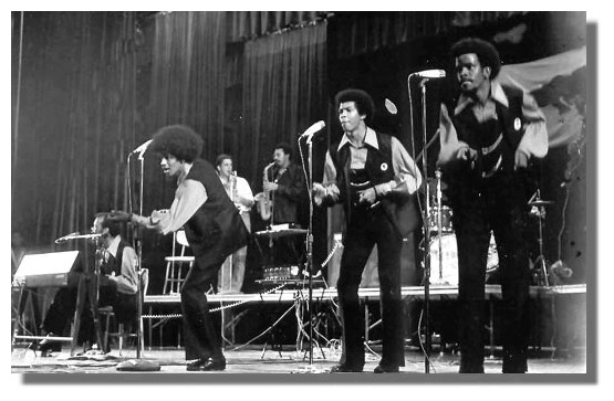 a black and white photo of a Black band performing and singing on stage