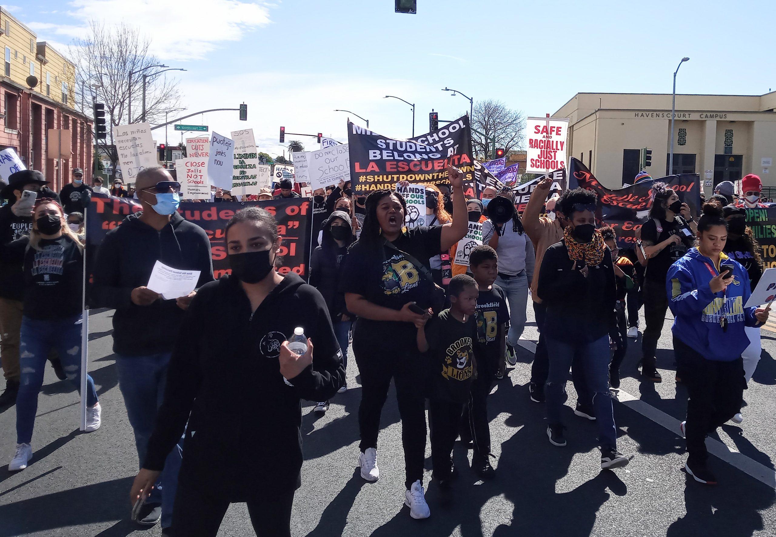 a throng of protestors, including children, march down East Oakland street holding signs