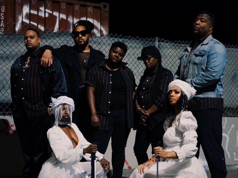 A group of African American band members, including two women wearing white dresses.