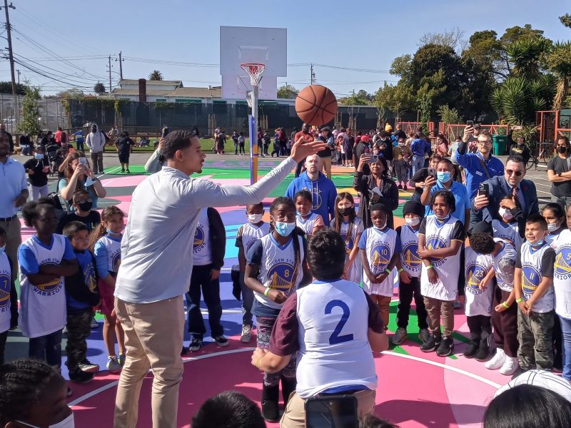 image of tall NBA player with mustache in new basketball court at elementary school, with a bunch of elementary kids surrounding him