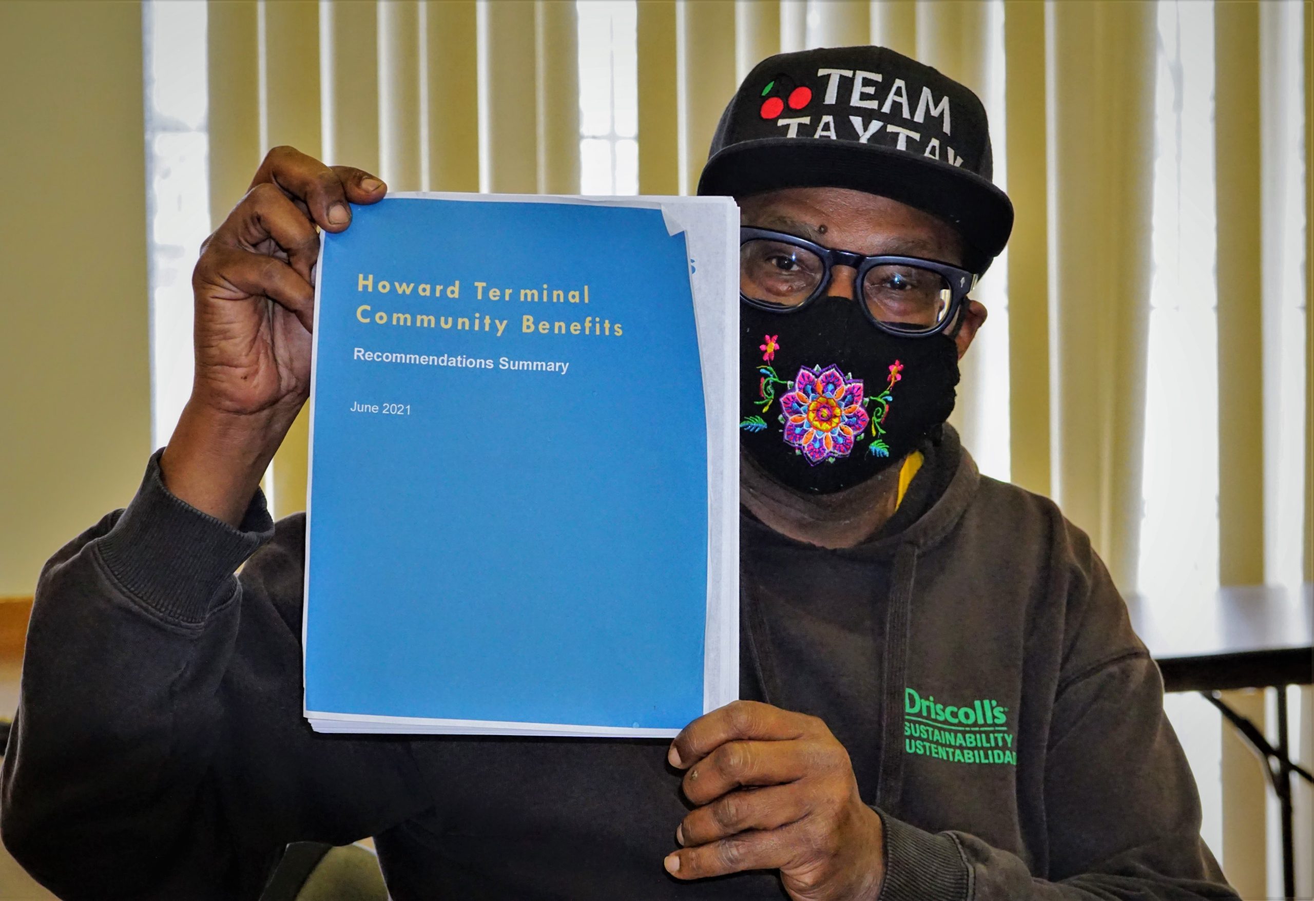 An African American man holds up a blue booklet that says Howard Terminal