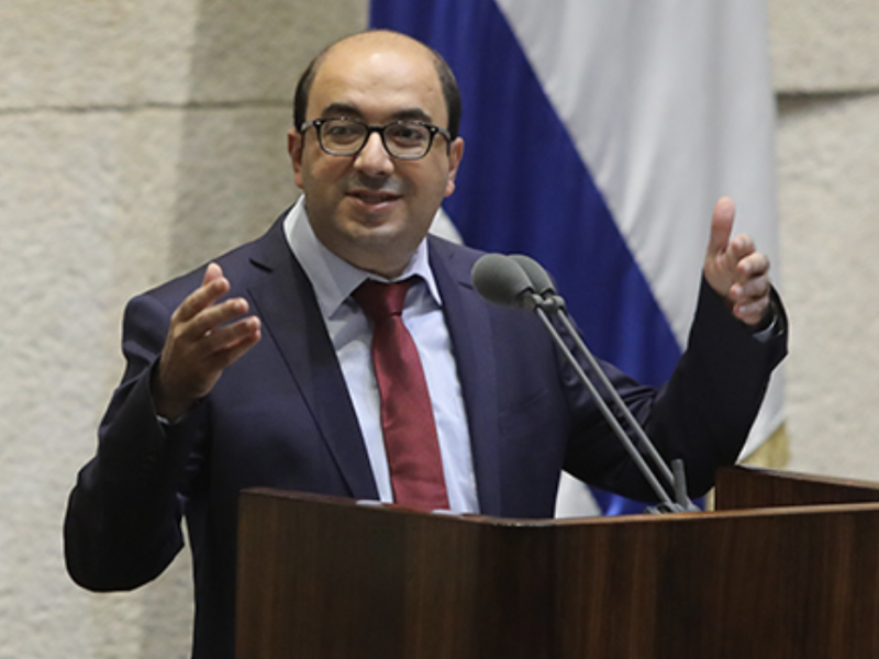 a man wearing glasses and a suit speaks at podium
