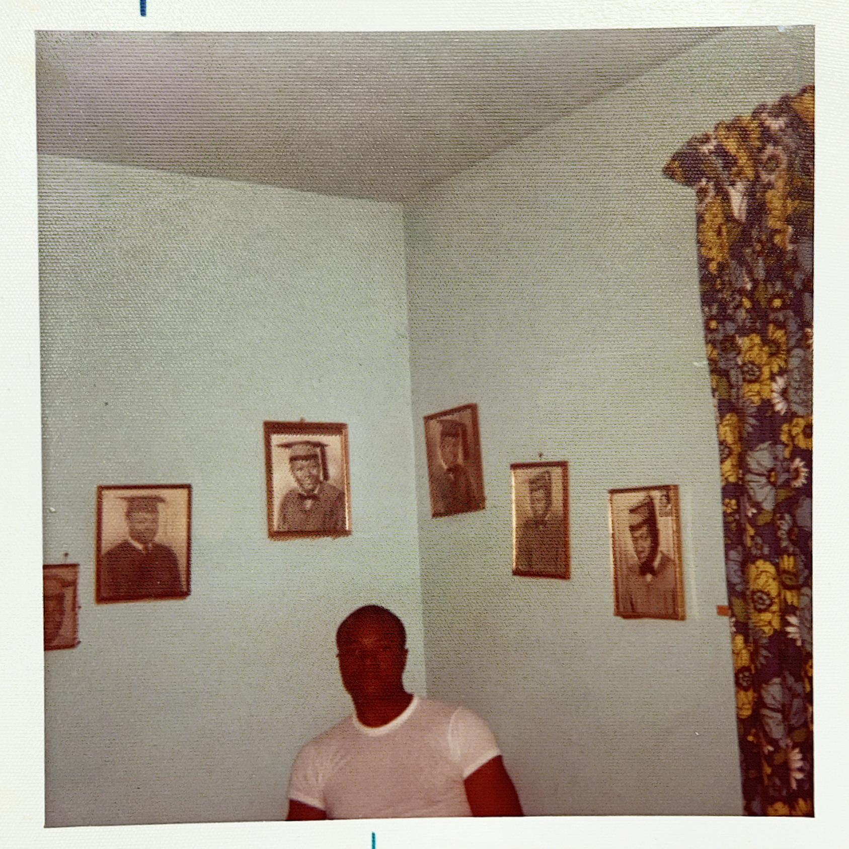 picture of man in white shirt sitting in corner of room surrounded by five framed photographs
