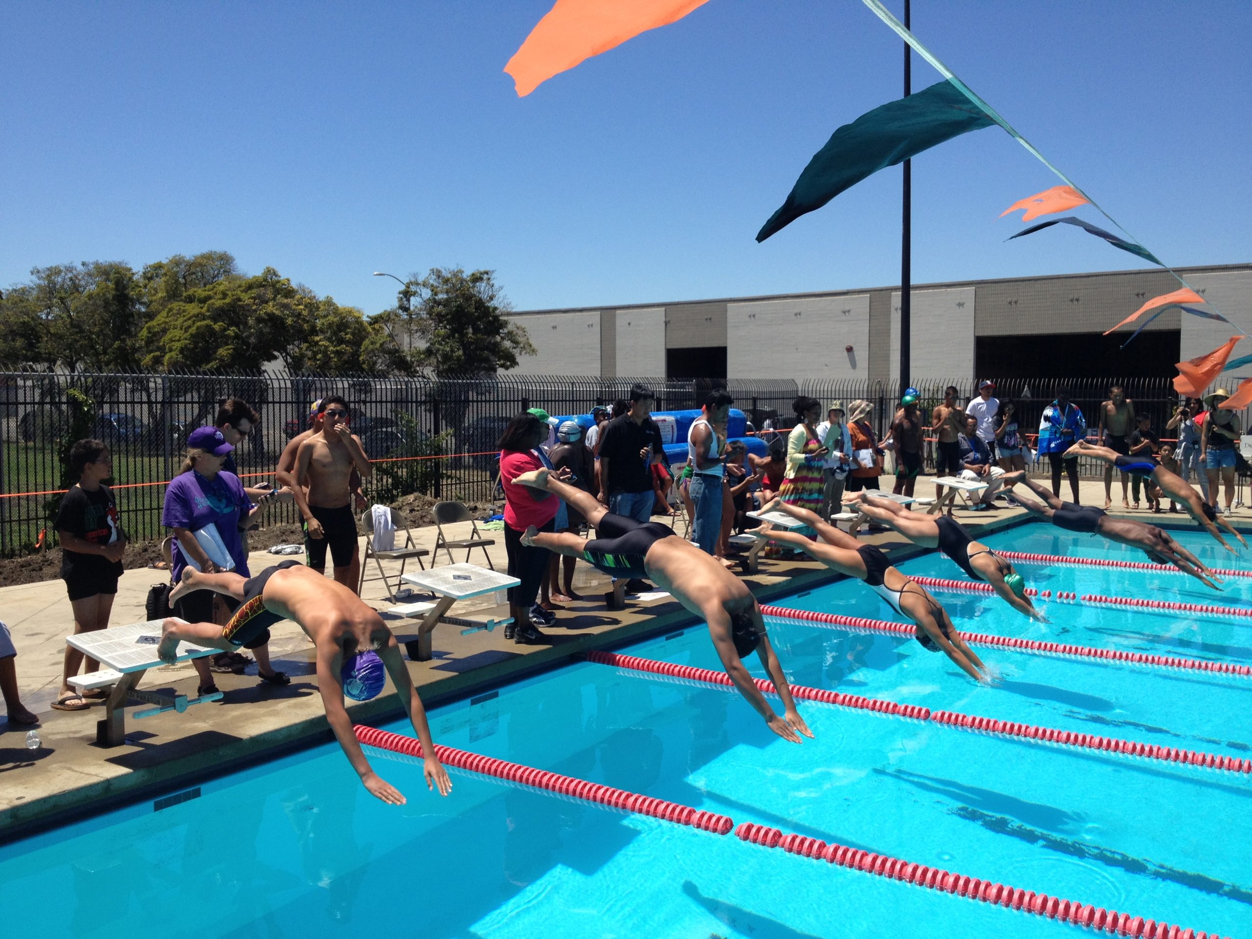 An aquamarine colored pool while divers in mid air jump into their swim lanes for a swim meet