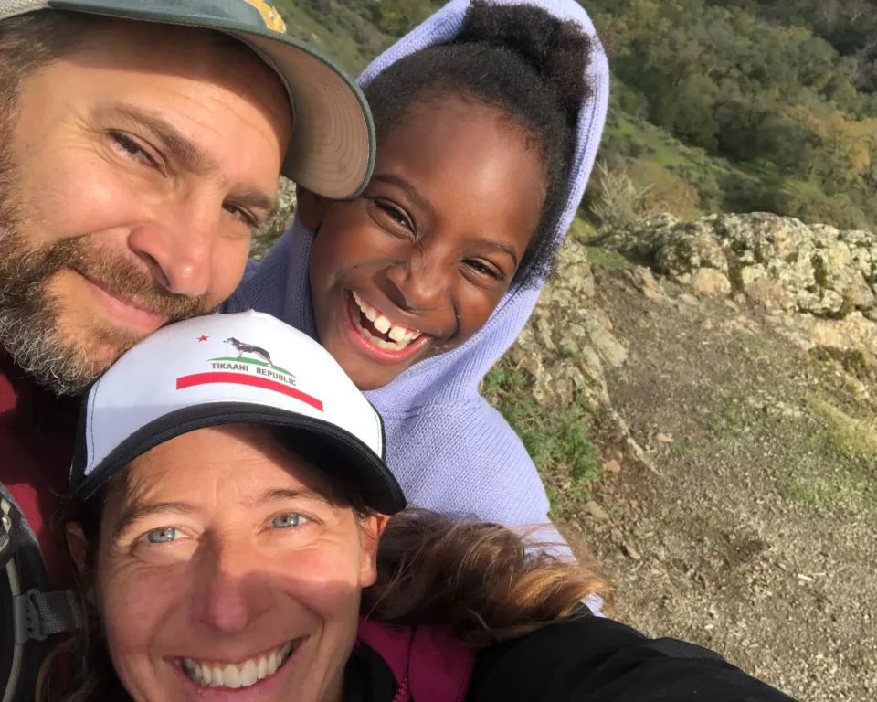 A woman with a man and child take a selfie outdoors. they are all smiling 