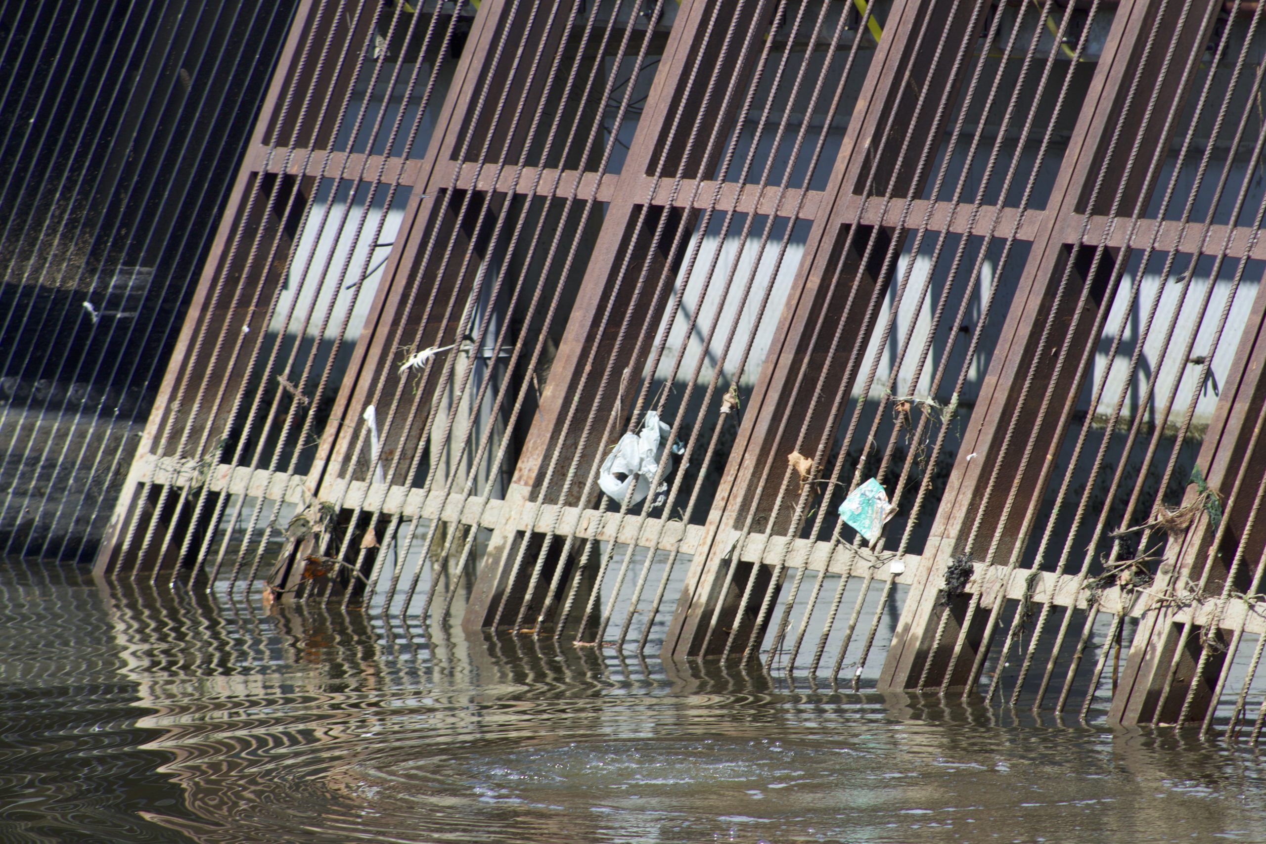 angled gates with some trash trapped on it and murky waters beneath