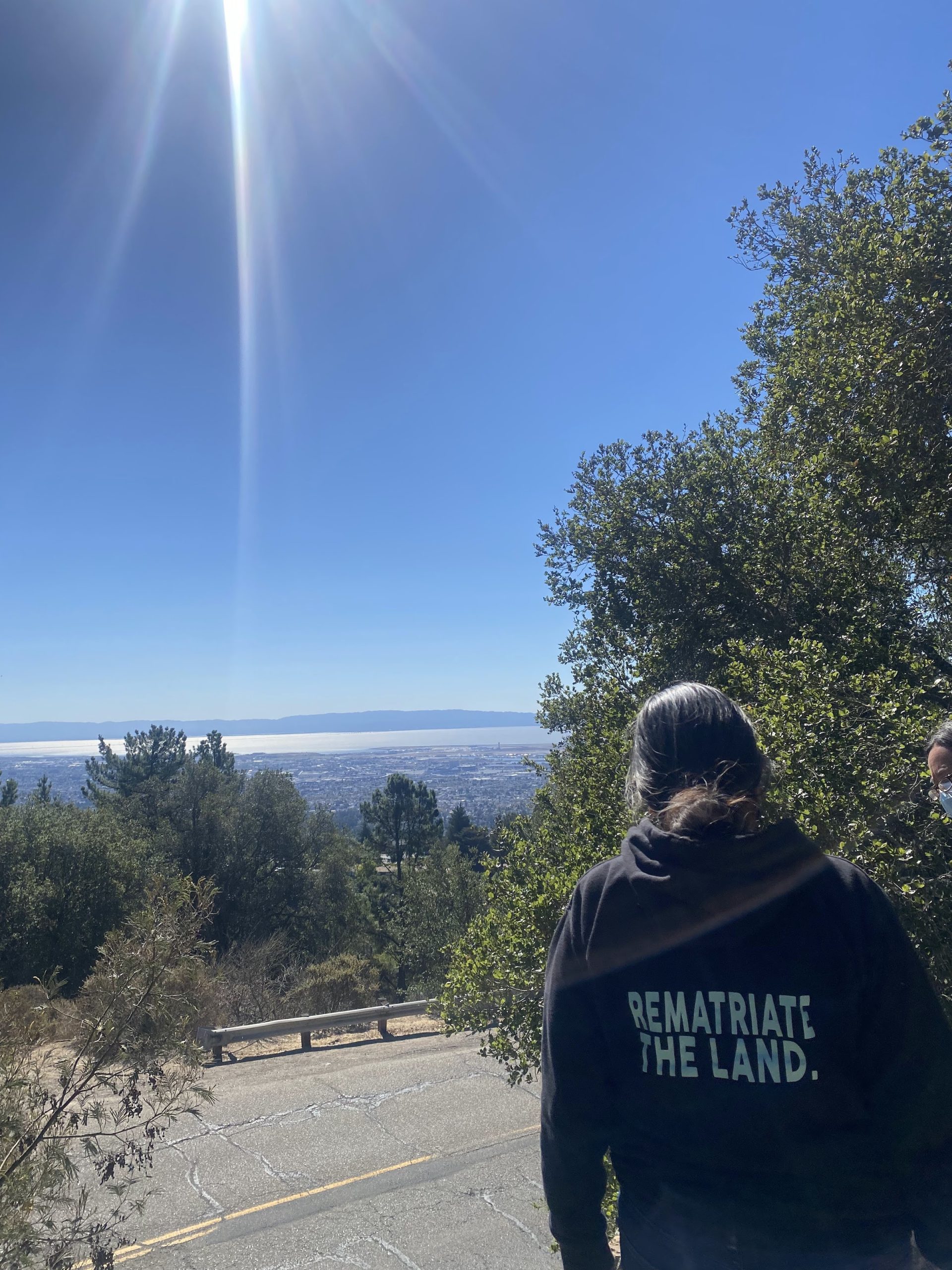 View from sunny hills, back of woman's black sweatshirt says "rematriate the land"