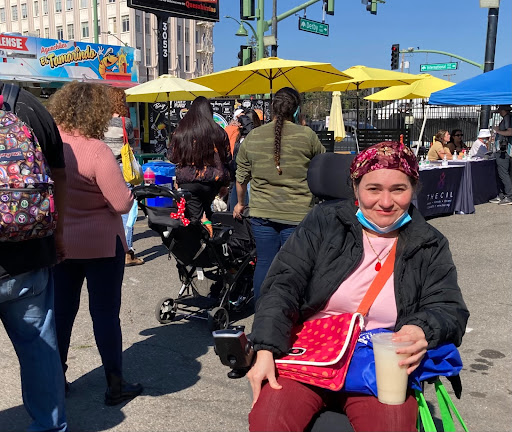A disabled Latine person sits in wheelchair during outdoor festival