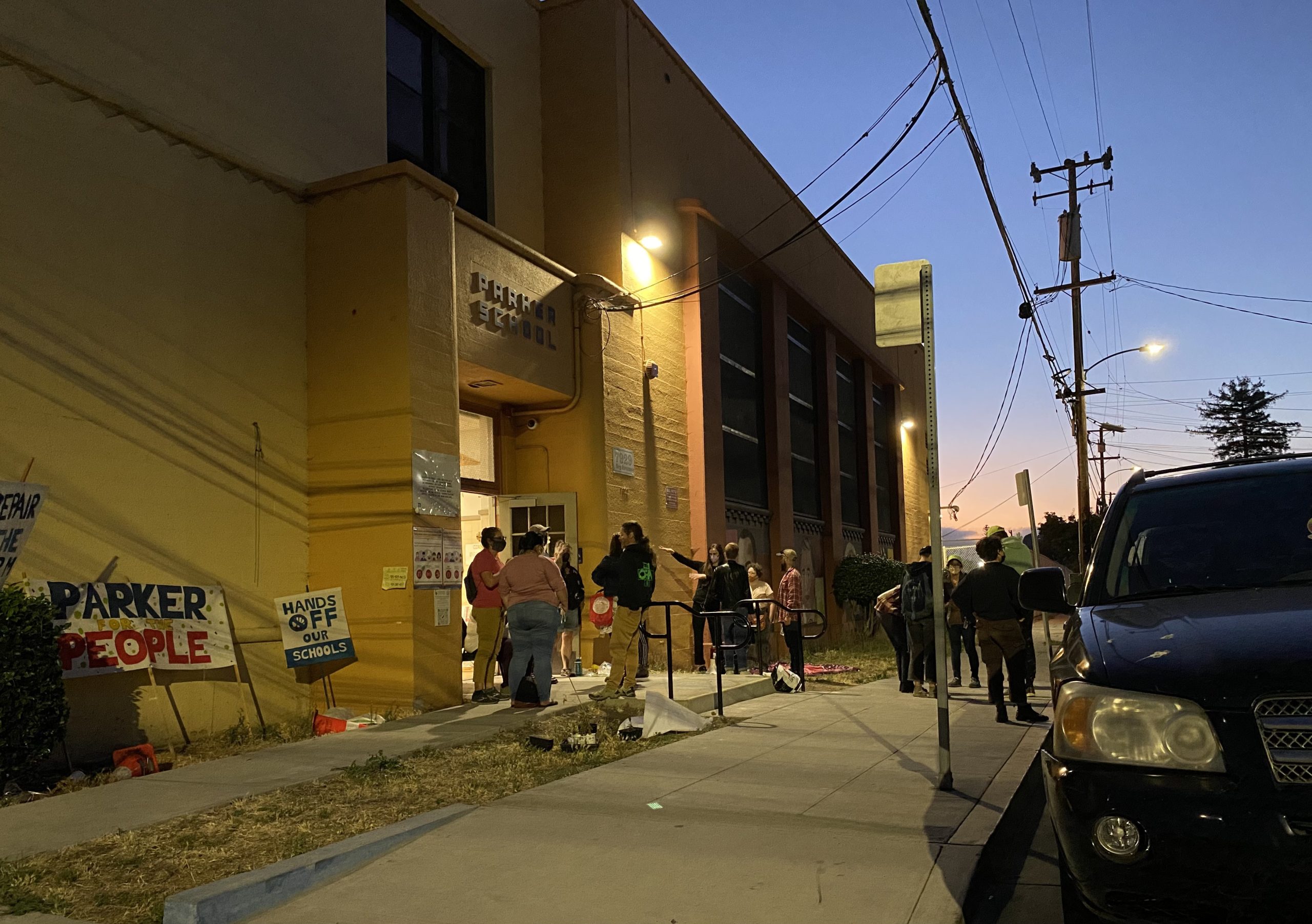 Nightime outside of a yellow school building with some people milling about outside