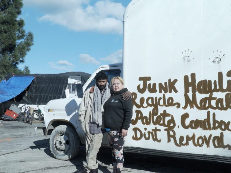 two people stand in front of a white truck that has hand lettering on it saying "junk hauling, metal..."