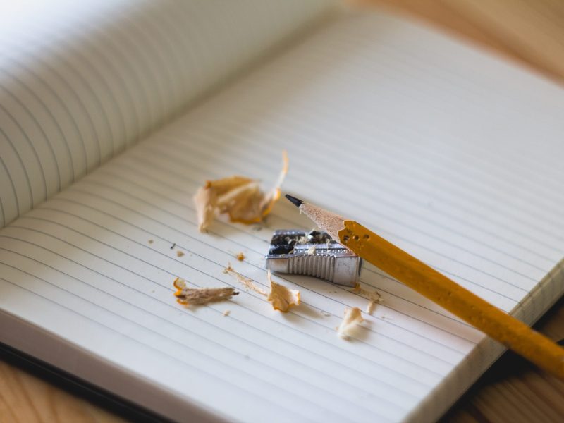 a broken pencil with handheld sharpener over a blank composition book