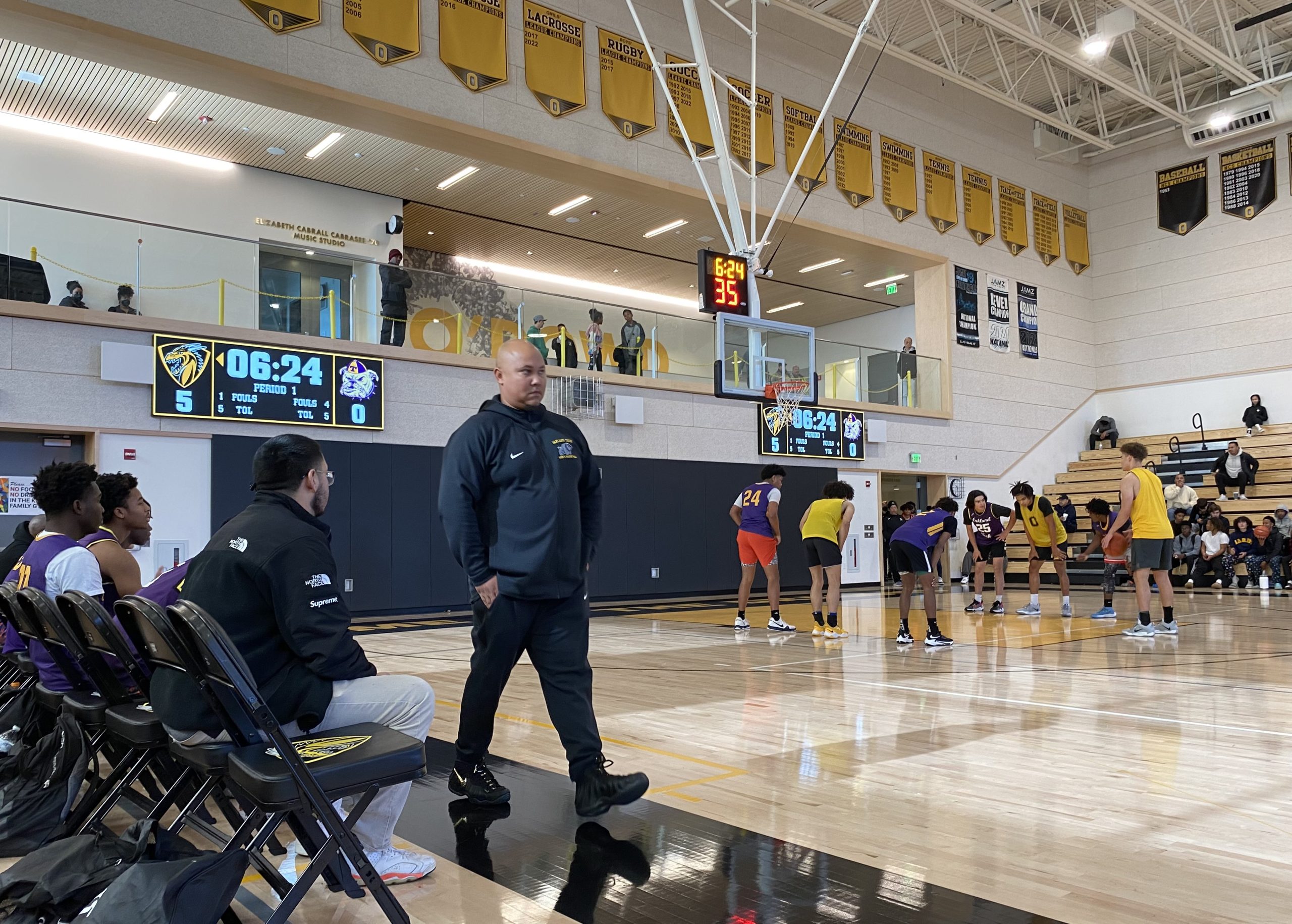 A male coach dressed in black athletic wear paces sidelines of new basketball court