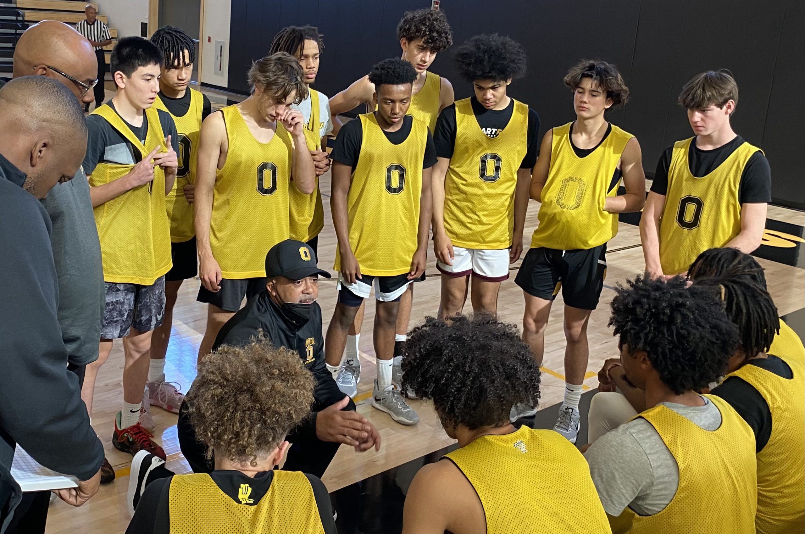 A group of boys basketball players in yellow tank tops huddles around their coach