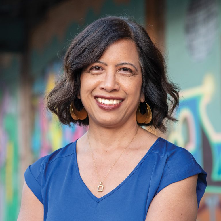 A Filipina American woman with short wavy brown hair smiles for camera