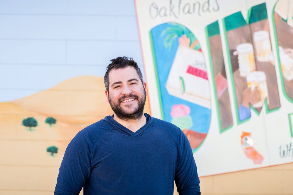 A man wearing a navy blue shirt and with a beard smiles at camera
