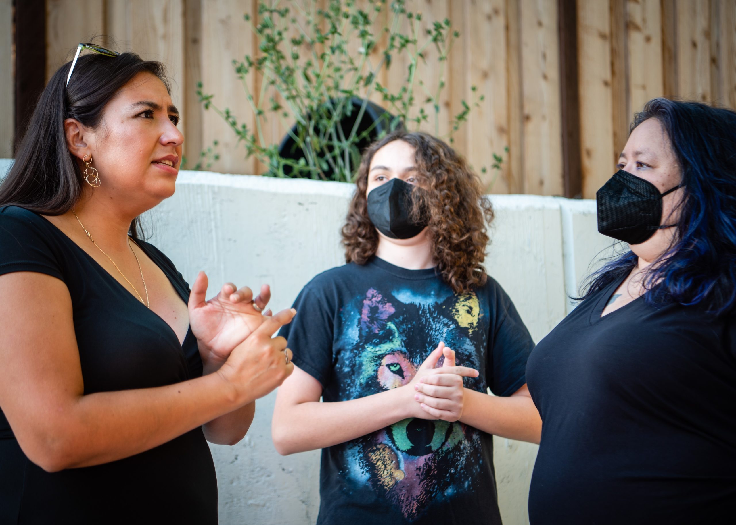A woman with dark brown hair talks with two people who are wearing masks