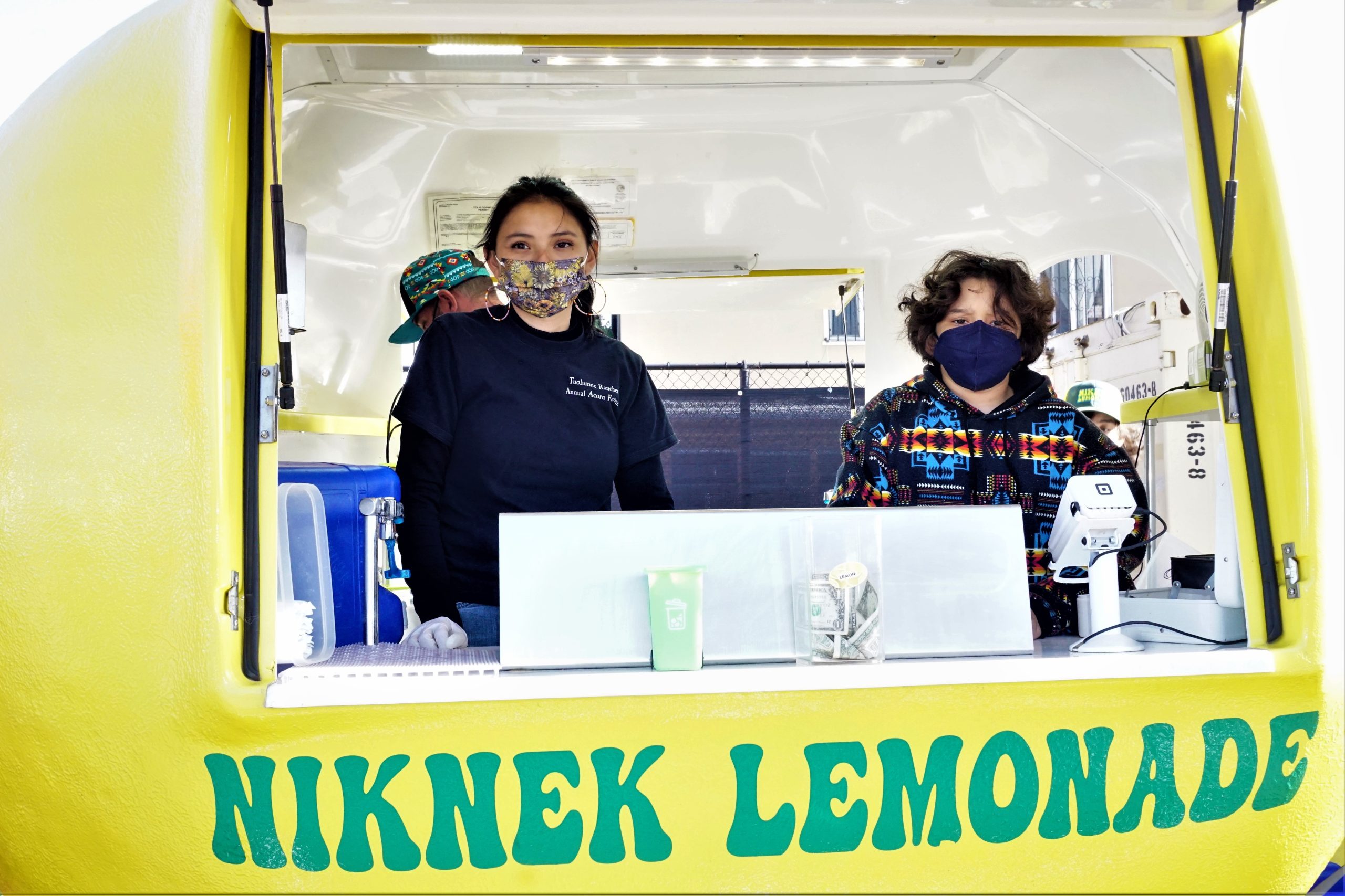 An image of two women behind a yellow food truck lemonade stand