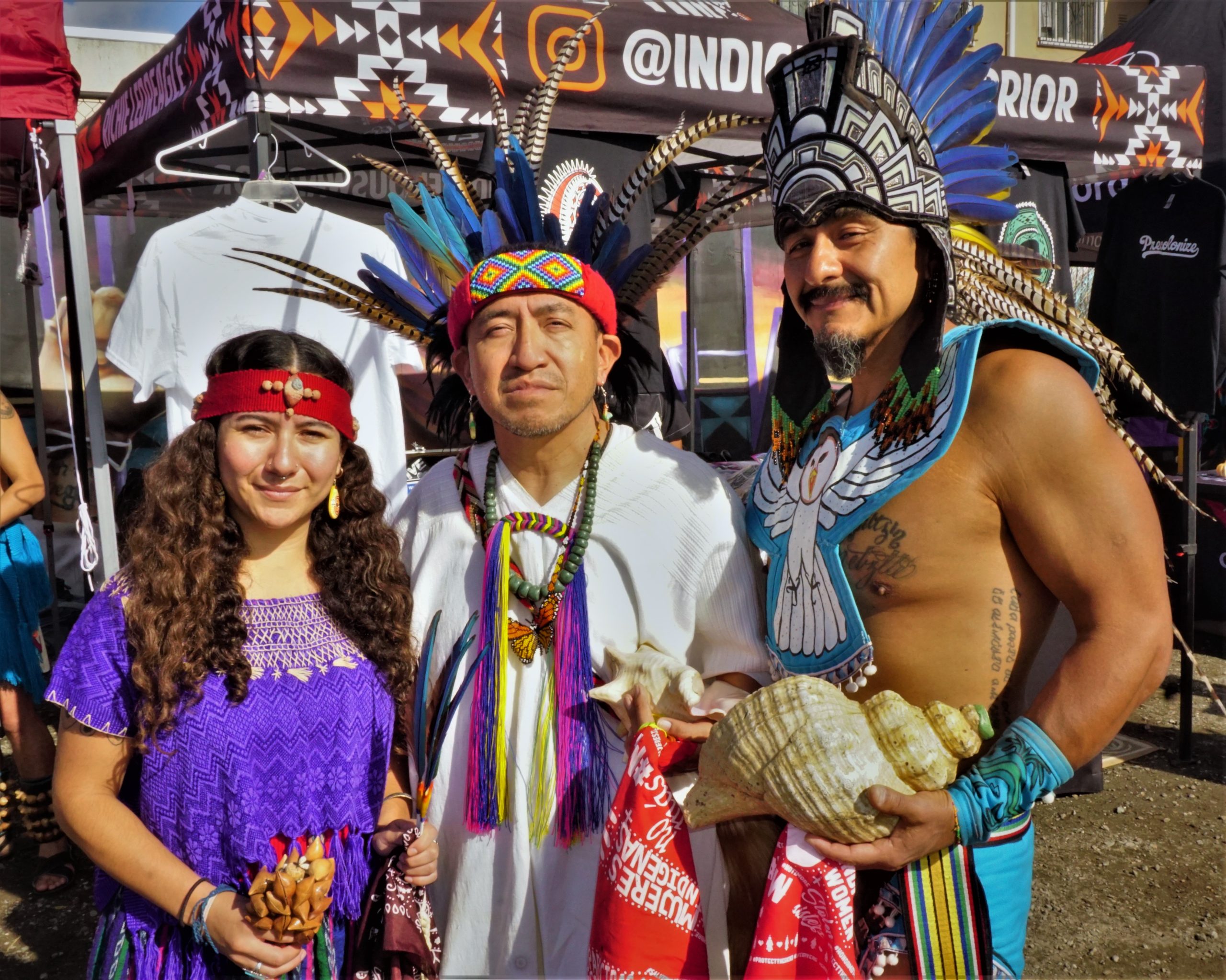 Calpulli Coatlicue Aztec Dancers wearing head dresses pose for photo at outdoor market
