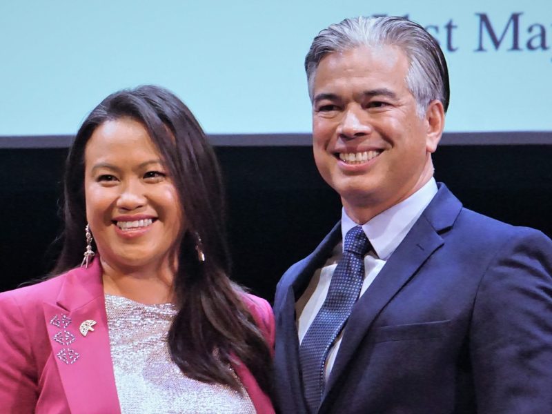 A Hmong American woman stands next to a Filipino American man on stage at the inauguration ceremony