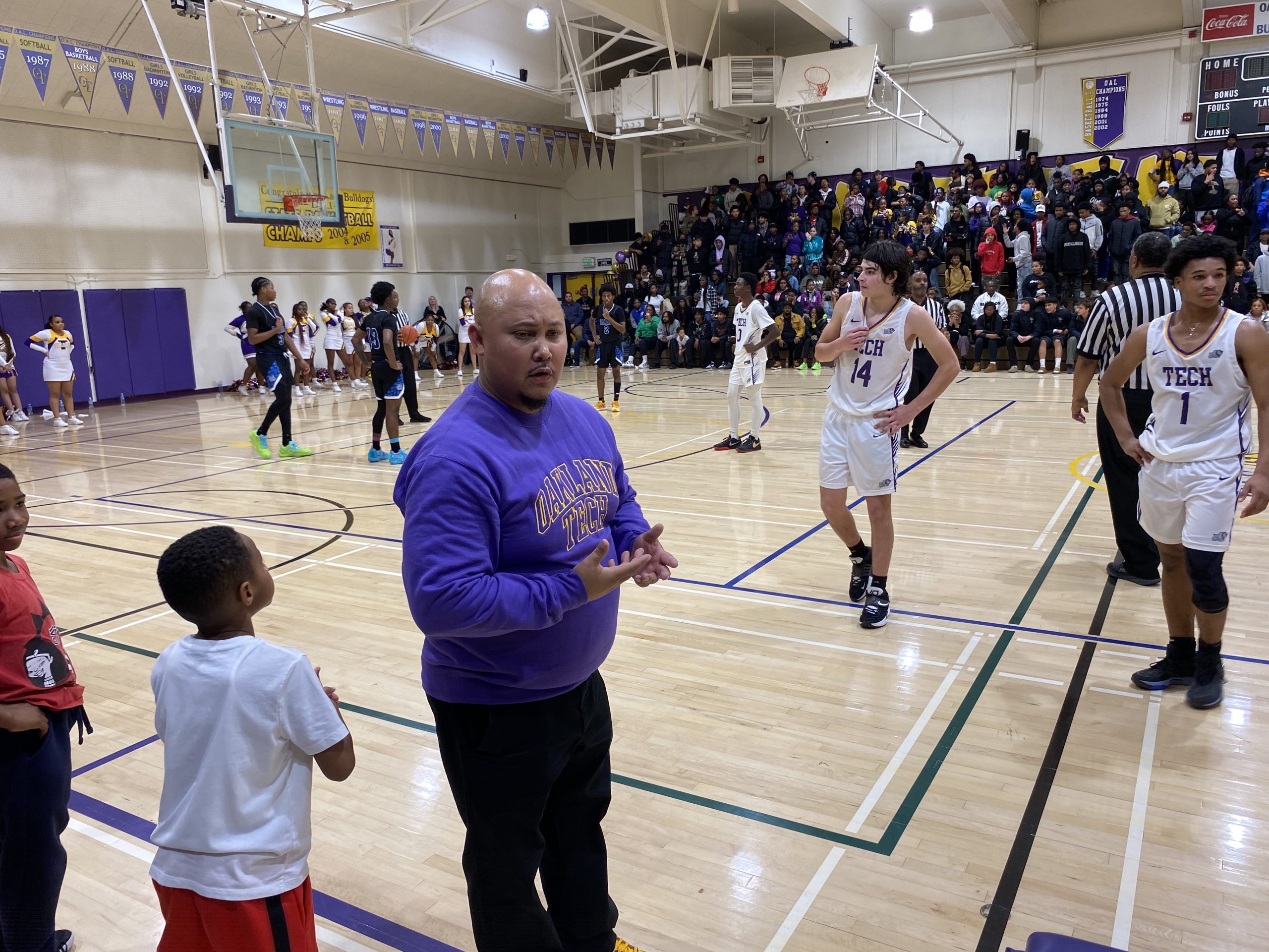 An Asian American man wearing a purple sweatshirt that says "Tech Bulldogs" is coaching a basketball game