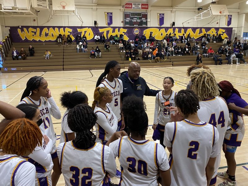 A group of basketball players surround a coach in an indoor game