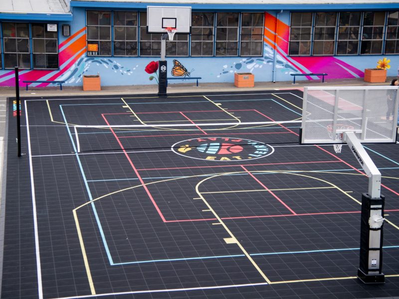 An aerial photo of a black basketball court that says "Eat. Learn. Play." in colorful font