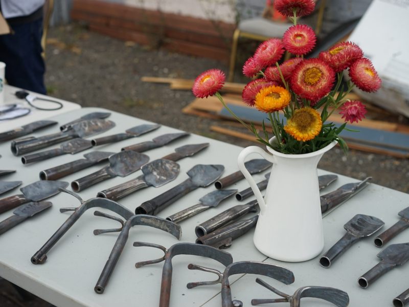 a table with gardening tools, along with a vase of red and orange flowers