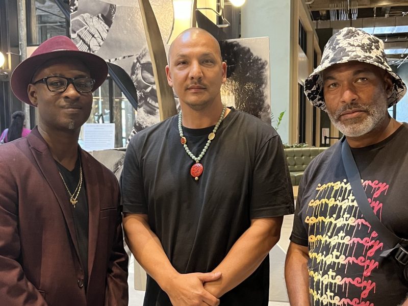 three Black men stand inside a large art exhibit and station in Oakland
