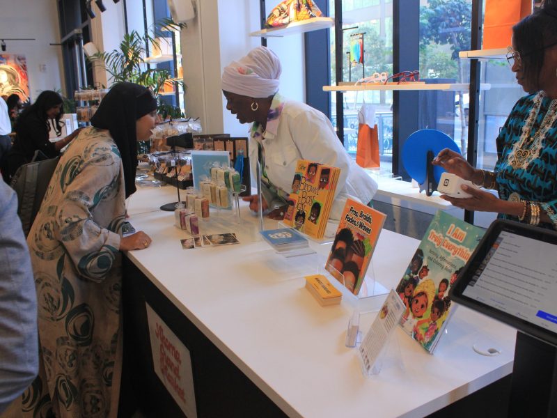 A woman wearing a head wrap shows another woman a book