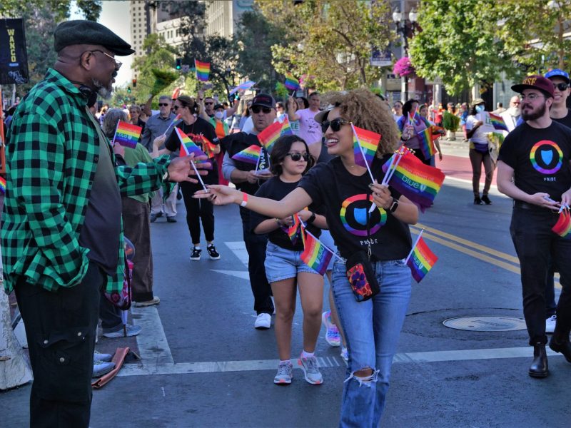 a Black woman passes out a rainbow flag to a Black elder man