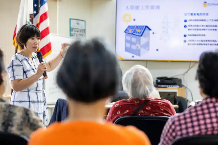 a Chinese American woman speaks into a mic in front of mostly Chinese elderly who live in an apartment complex