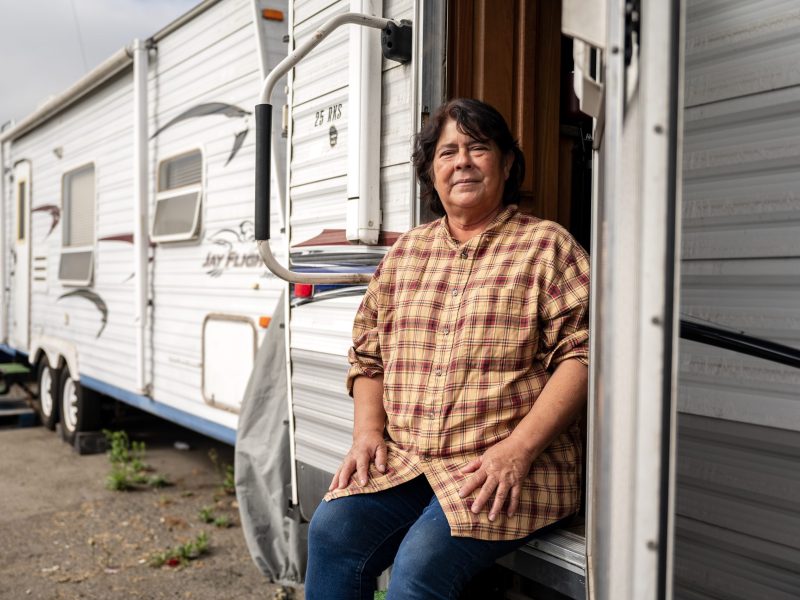 A woman sits on the front step of a trailer home