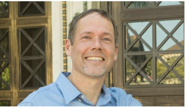 A white man wearing blue collared shirt smiles for camera