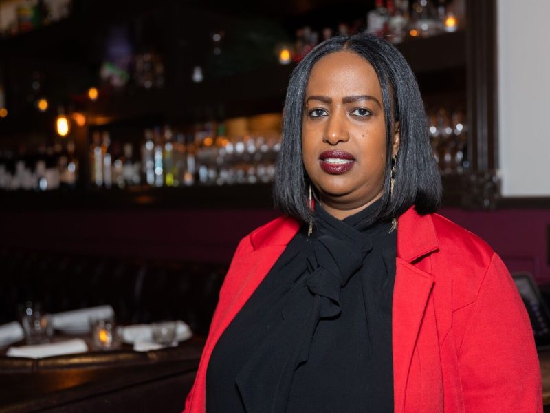 An African American woman with short straight hair wearing a red jacket poses for photo inside her restaurant