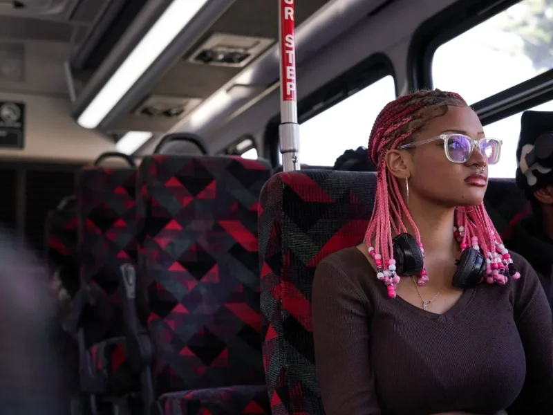 An African American girl sits inside a bus looking outside the window