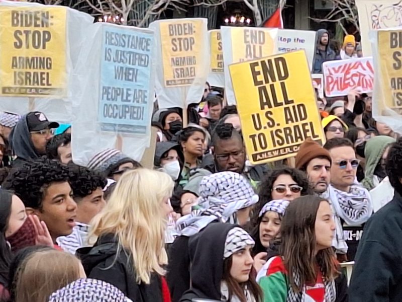 a diverse group of people holding protest signs about Israel's attack on Gaza