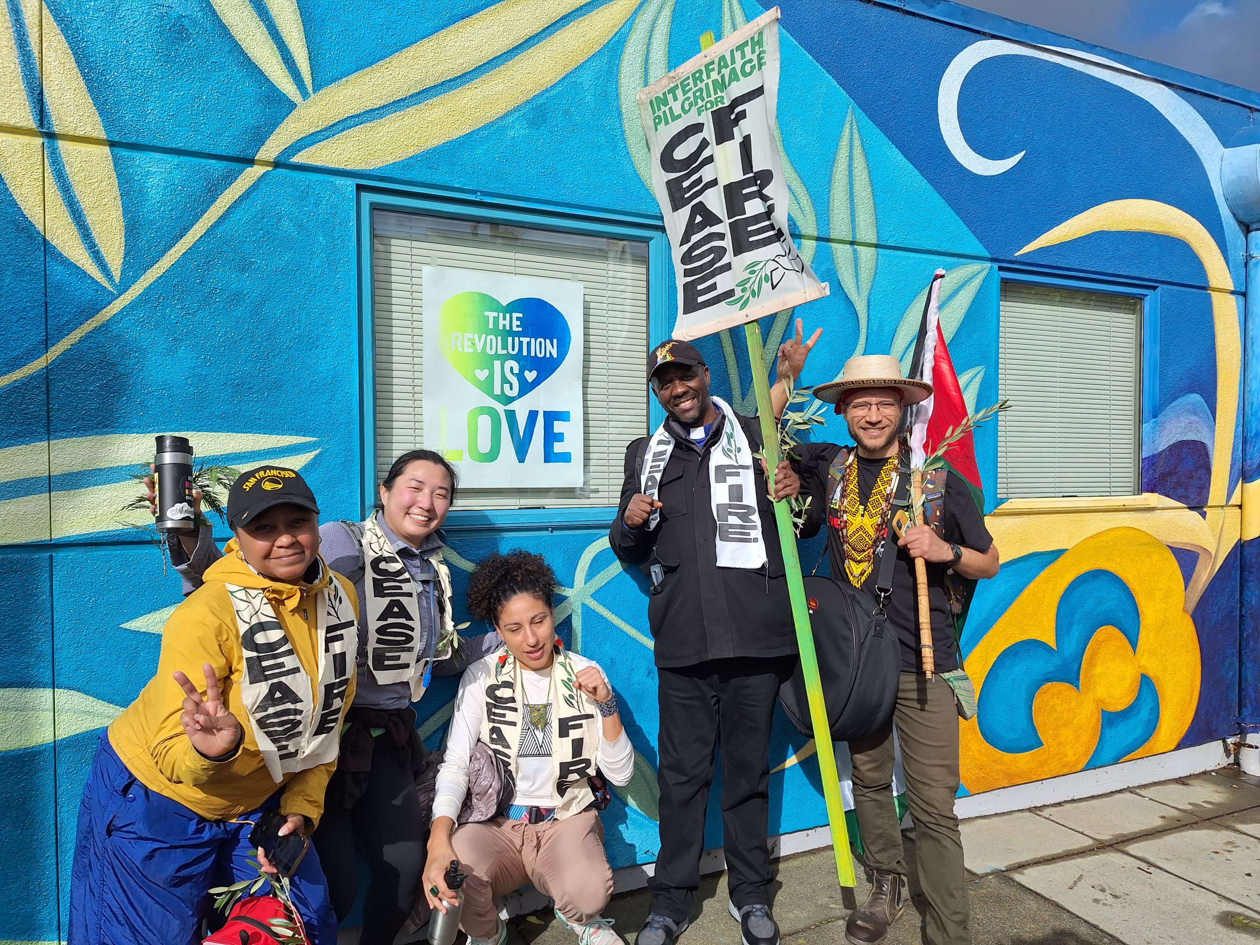 A group of diverse people holding placard and signs for ceasefire in front of a colorful wall